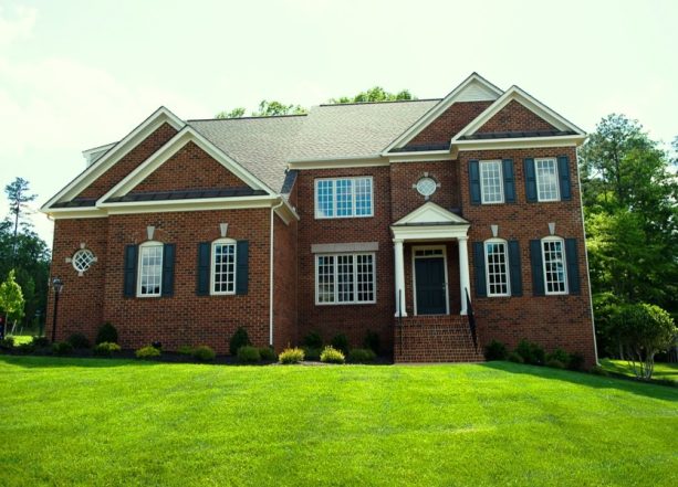 a big traditional house that has a working mix of navy blue shutters concealing white window frames and walls of red bricks