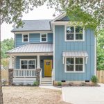 a coastal light blue vinyl exterior house with a yellow door and a mixed material roof
