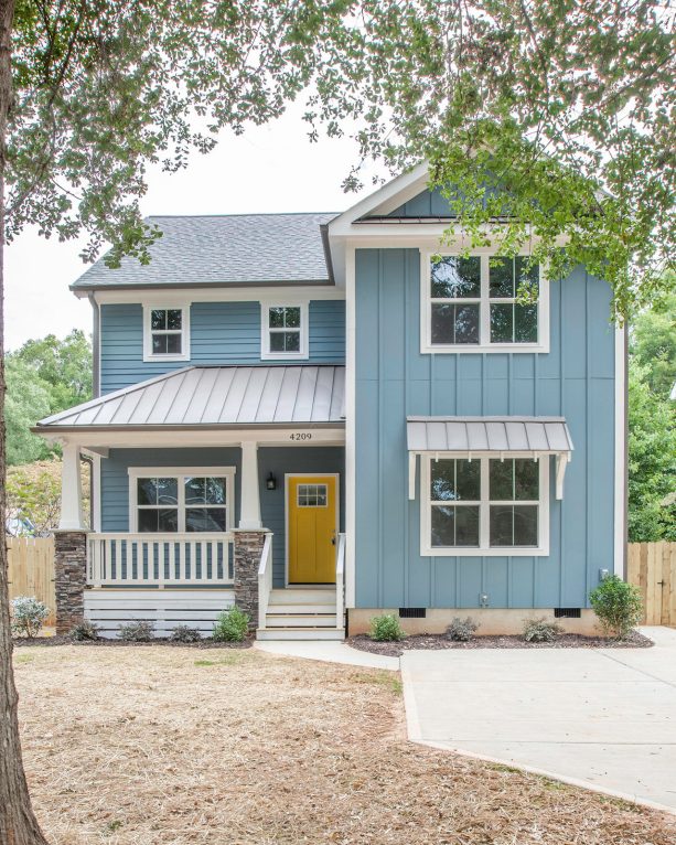 a coastal light blue vinyl exterior house with a yellow door and a mixed material roof
