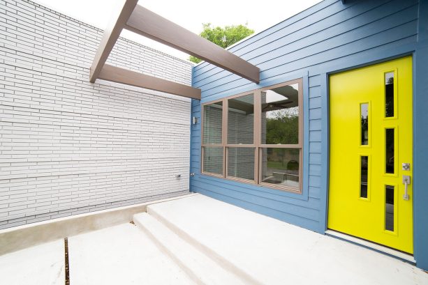a contemporary blue house with dark gray window frames and a modern yellow glass-front door