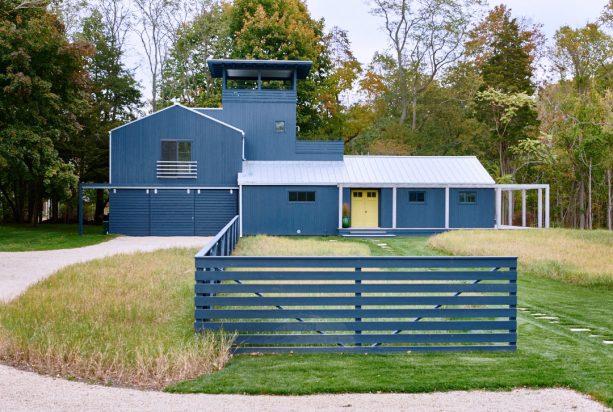 a navy blue two-story farmhouse with a yellow front door and a silver metal roof