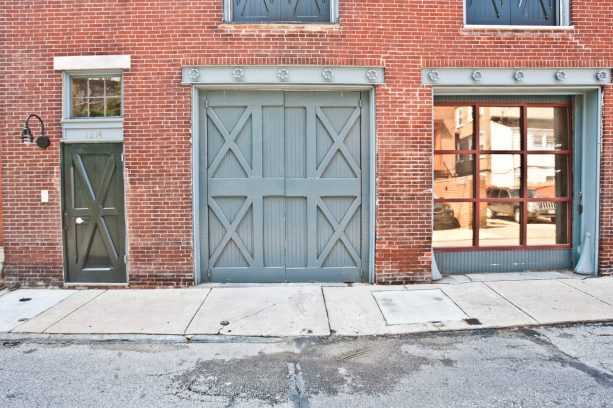 a pair of large grey double front doors and matching window shutters with an exposed brick wall are the things an eclectic exterior needs the most
