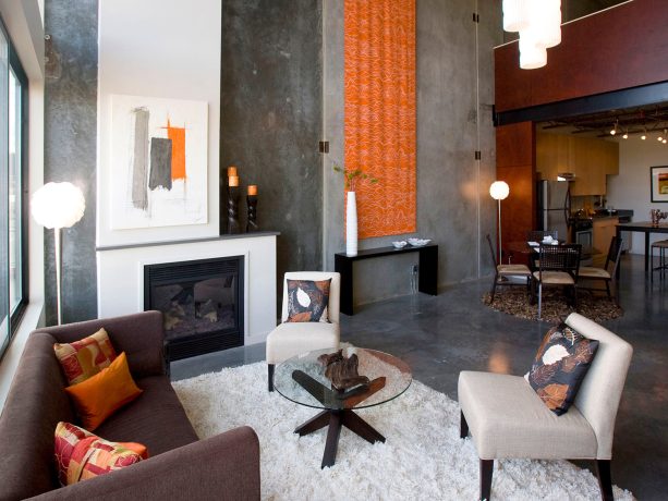 an industrial living room can benefit from the presence of a grey floor and matching concrete walls decorated with an interesting orange fabric