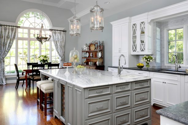 luxury is brought into a kitchen when white and gray cabinets are supported by gray walls throughout and accents of shiny brown coming from a hardwood floor and wooden furniture pieces