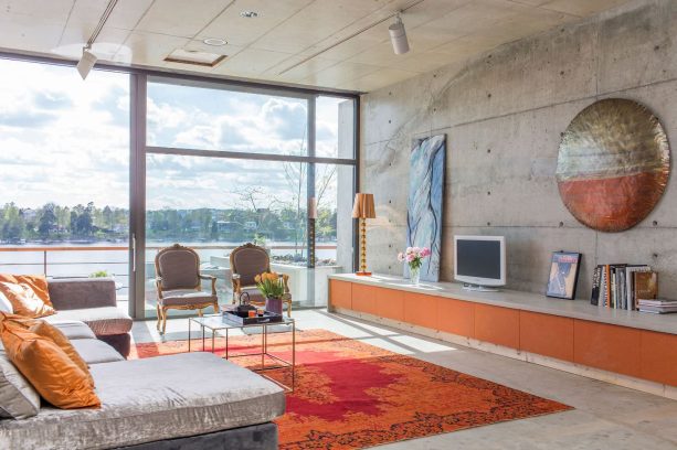 orange and red that hang around with each other on an area rug is the accent colors that a living room with gray concrete walls and floor needs