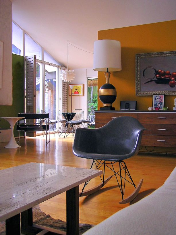 orange walls and a grey rocking chair are excellent choices for a living room that loves its midcentury origins