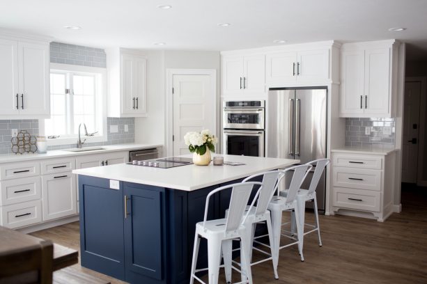 a kitchen with a navy island and white shaker cabinets accentuated by a grey backsplash