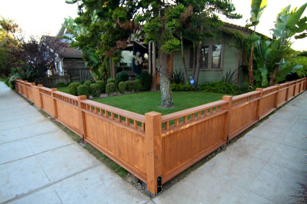 a low wooden fence protecting a grass yard with a tree in the center makes for an unadorned yet stunning corner lot landscaping idea