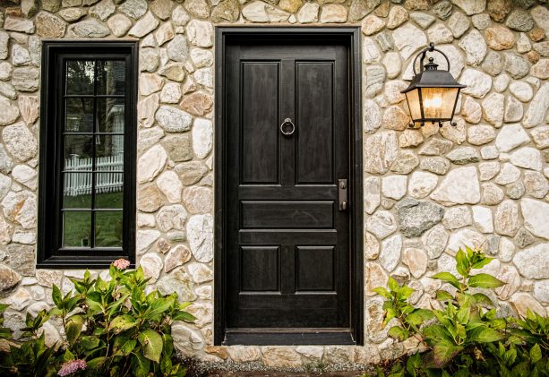 black colonial front door surrounded by stone wall exterior