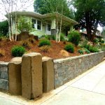 it’s a unique landscaping idea to construct a corner lot with a retaining wall and three large stone columns