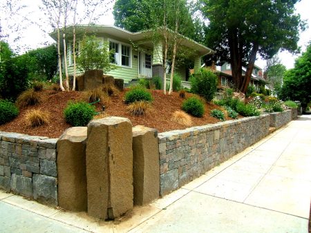 it’s a unique landscaping idea to construct a corner lot with a retaining wall and three large stone columns