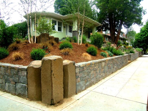 it’s a unique landscaping idea to construct a corner lot with a retaining wall and three large stone columns