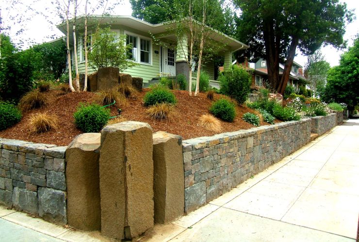it’s a unique landscaping idea to construct a corner lot with a retaining wall and three large stone columns