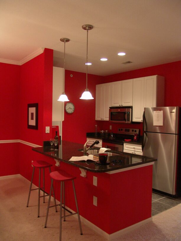 a galley kitchen with a red peninsula that has a black quartz countertop