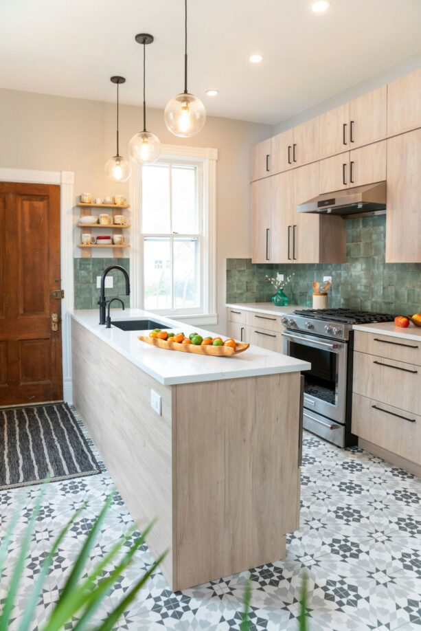 a light wood peninsula with a quartz countertop in a galley kitchen with porcelain tiles